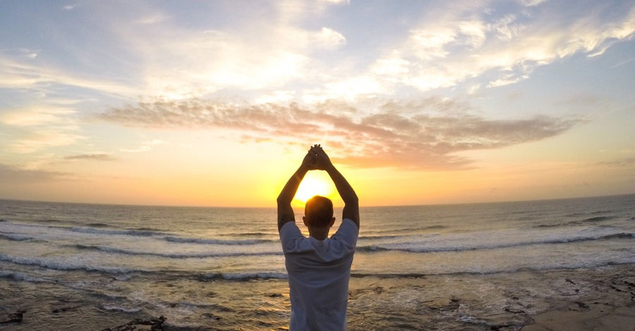 Man stretching on beach with sun between his arms