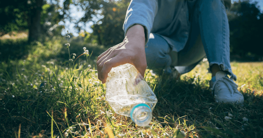 Hand picking up a plastic bottle from the ground