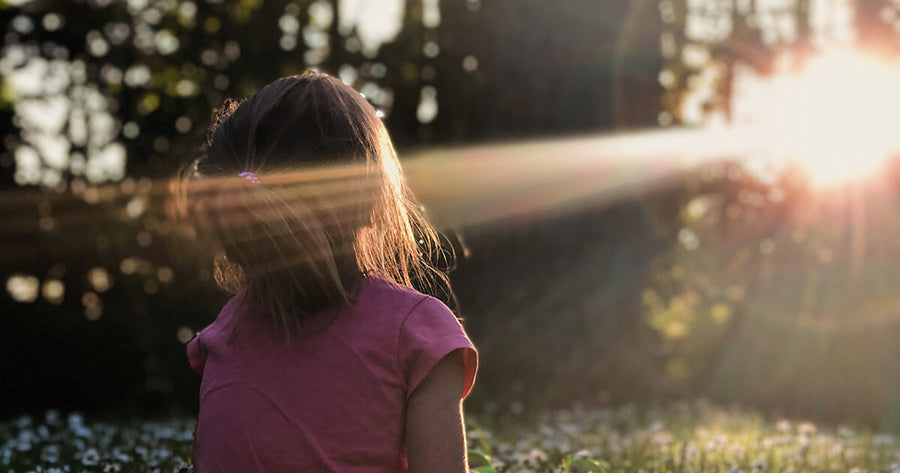 Child sitting in nature looking towards sun