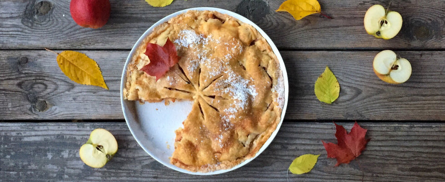 Pie in pan dusted with sugar surrounded by leaves and halved apples