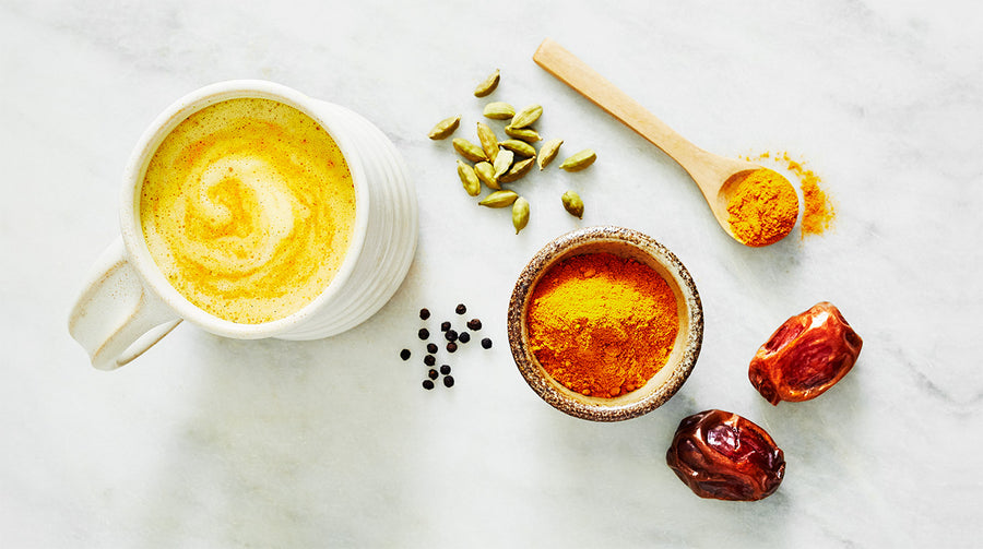 Golden Milk in a mug surrounded by dates, cardamon, turmeric and herbs